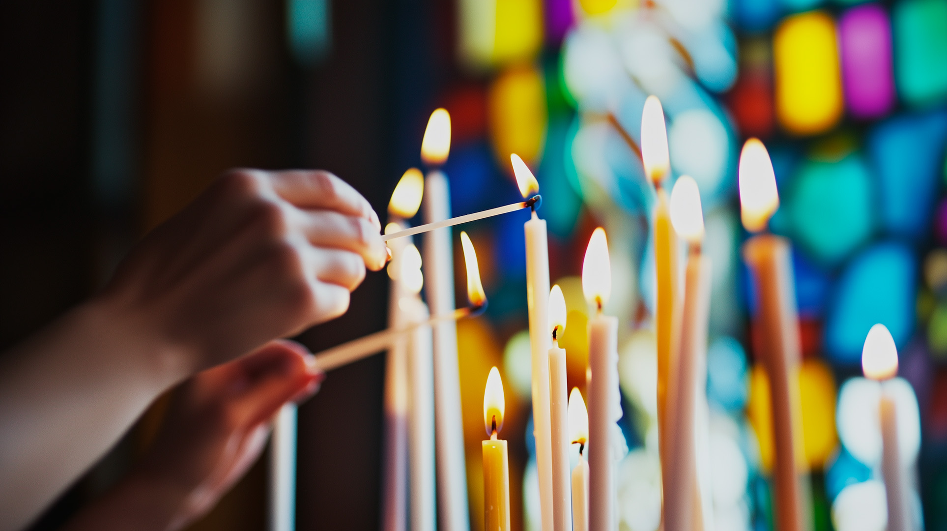 Händer tänder stearinljus med kyrkans mosaikfönster i bakgrunden