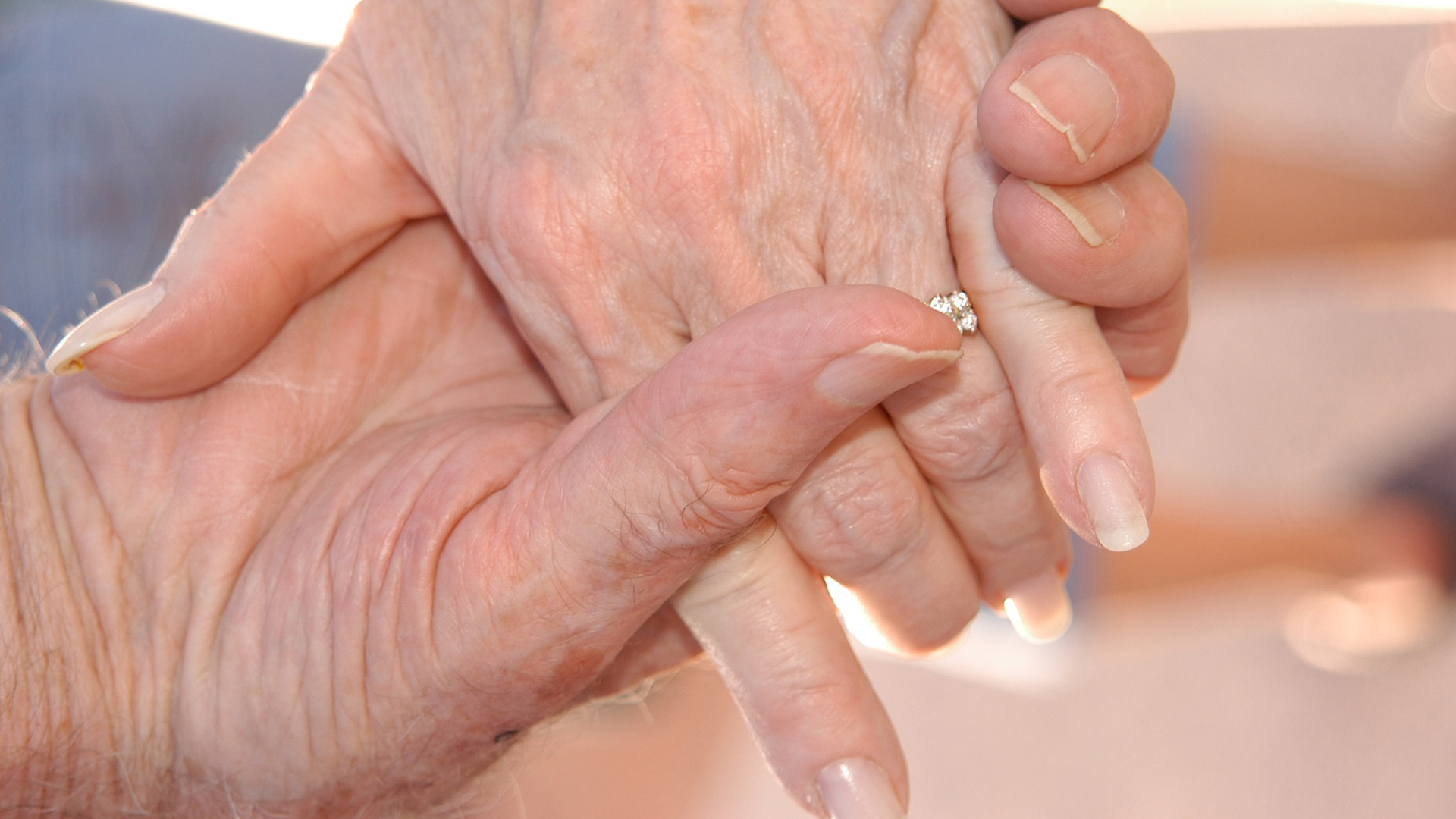 Två äldre personer håller varandra i handen - närbild på händerna