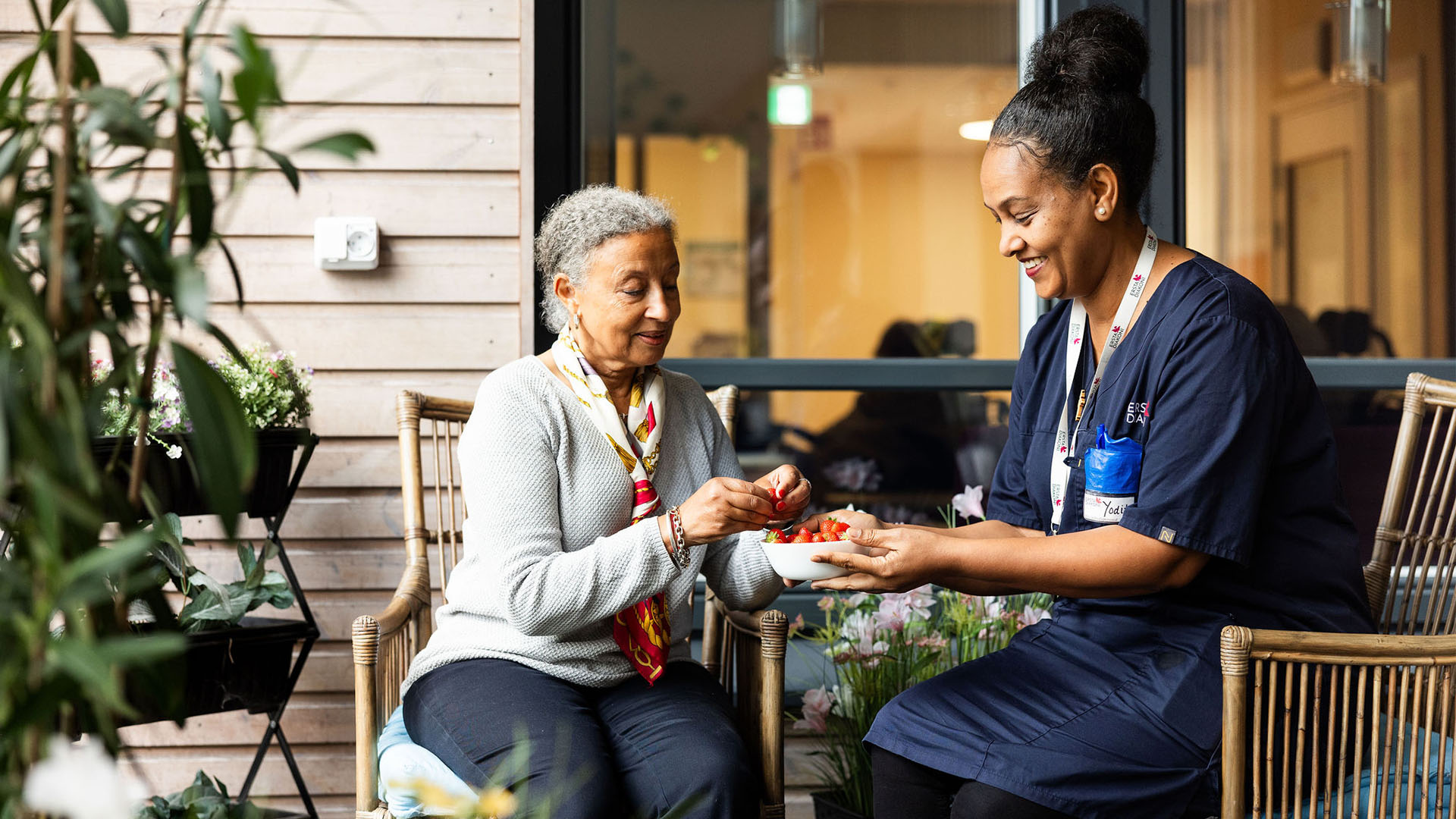 Tv&aring; ersoner, en &auml;ldre kvinna och en personal fr&aring;n Ersta &auml;ter jordgubbar p&aring; balkongen