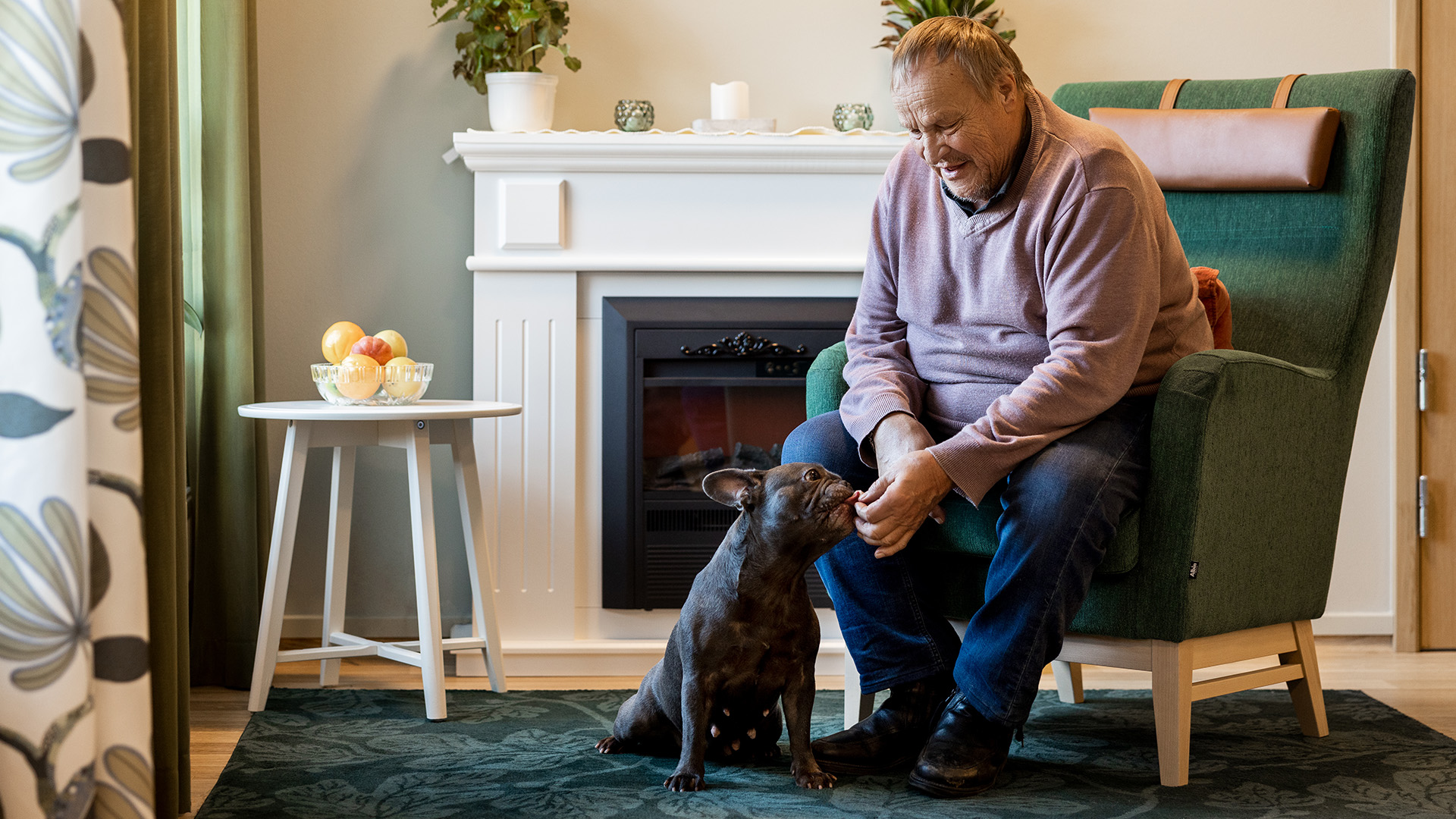 man vid en öppen spis klappar en hund som sitter på golvet