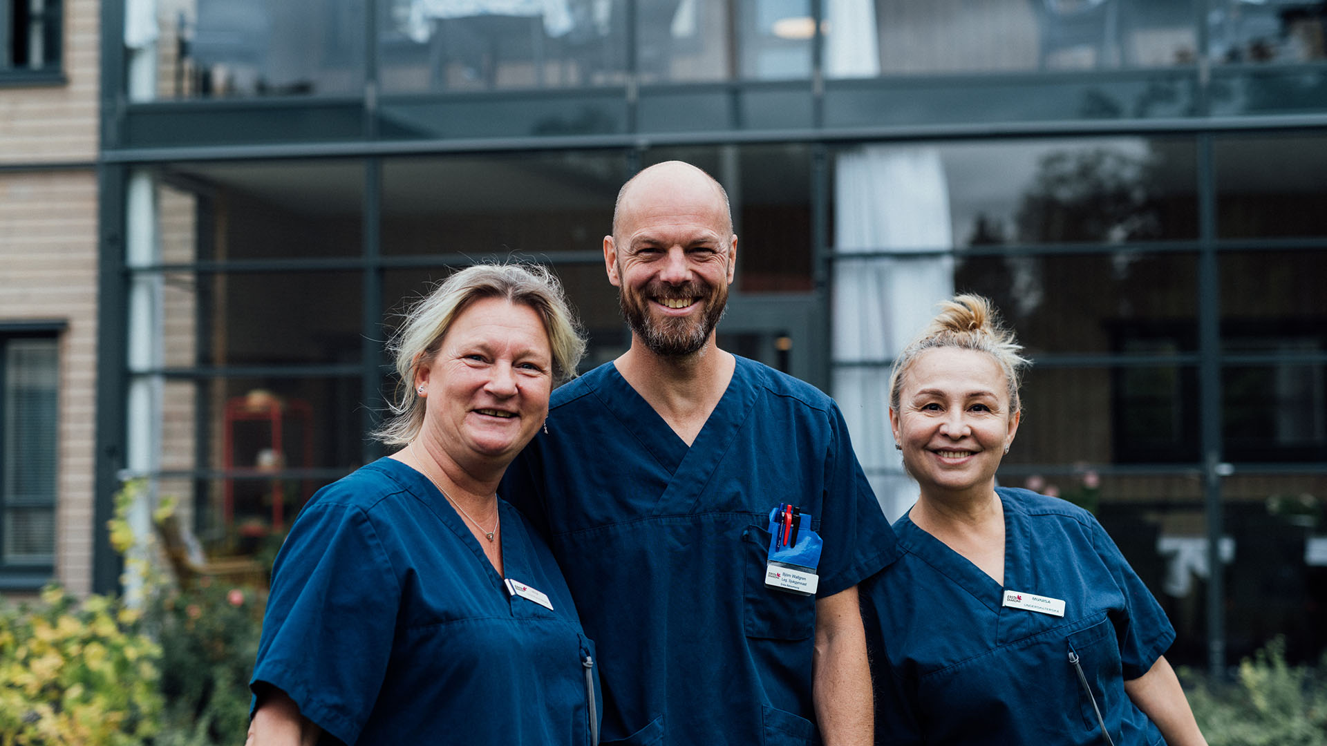 tre medarbetare på erstas äldreboende står tillsammans på en lummig gård