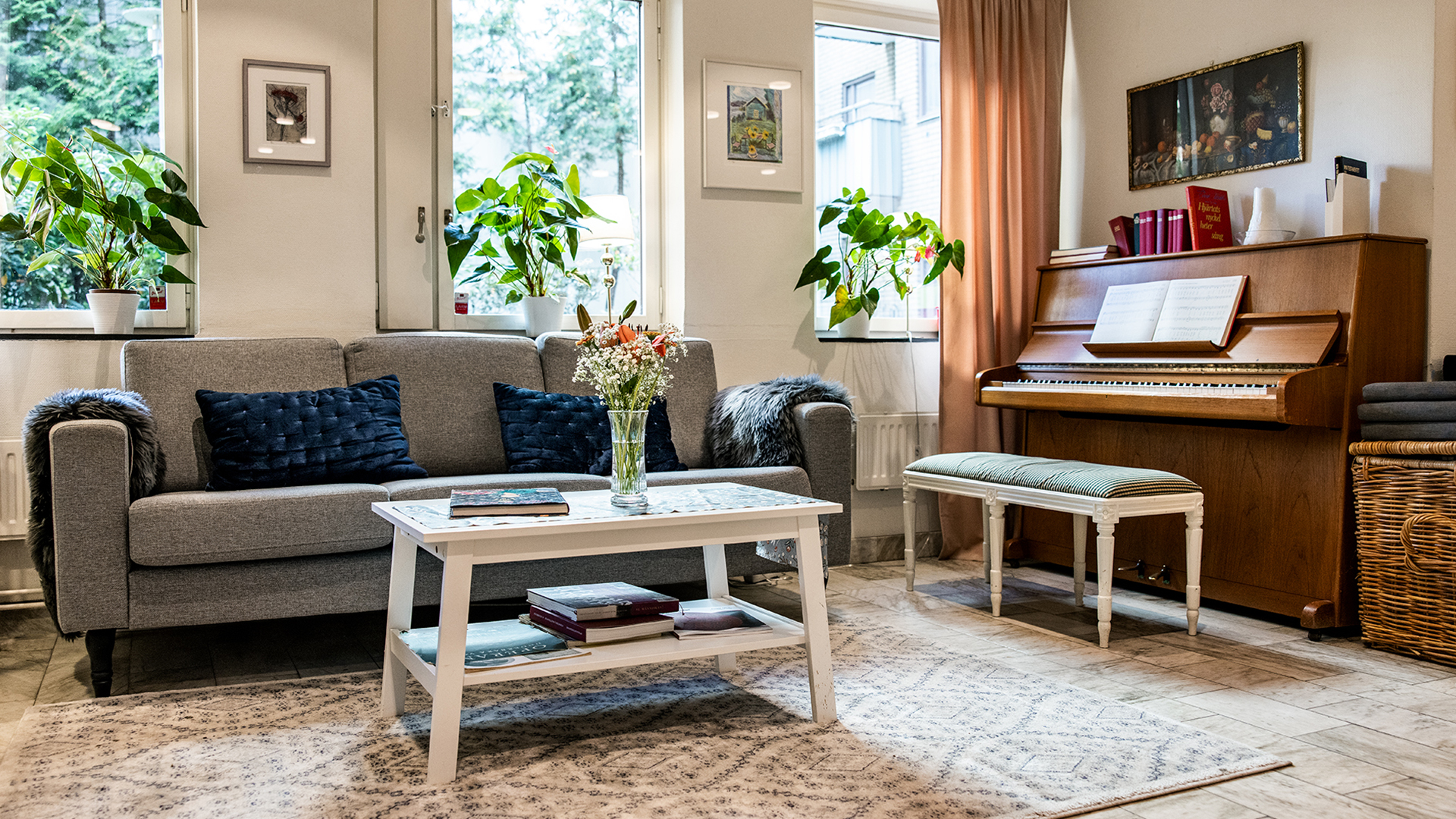 Linnégårdens gemensamma vardagsrum med grå soffa och ett piano