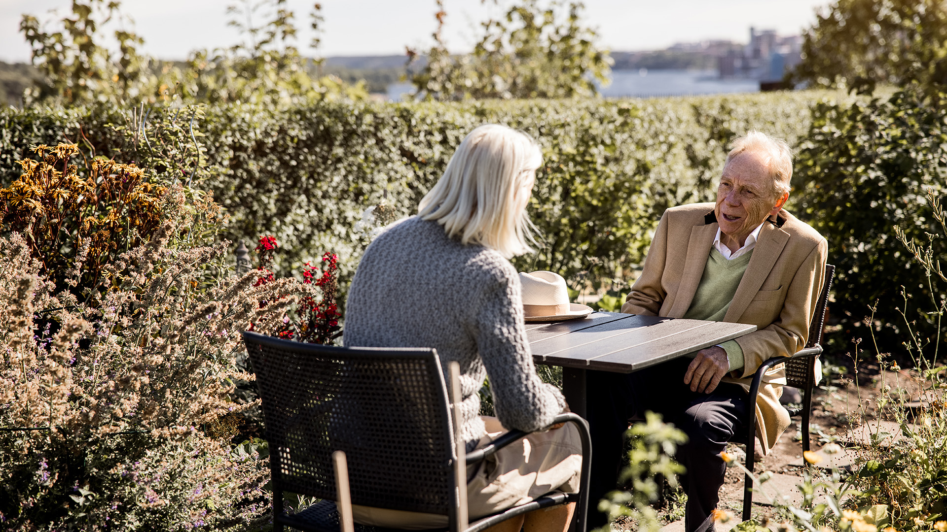 kvinna och man sitter i en vacker trädgård med utsikt över vatten