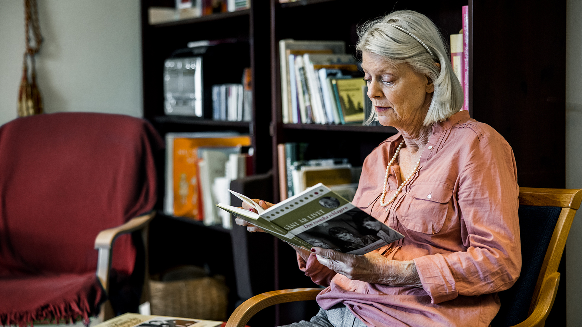 en äldre kvinna sitter i en stol och läser en bok
