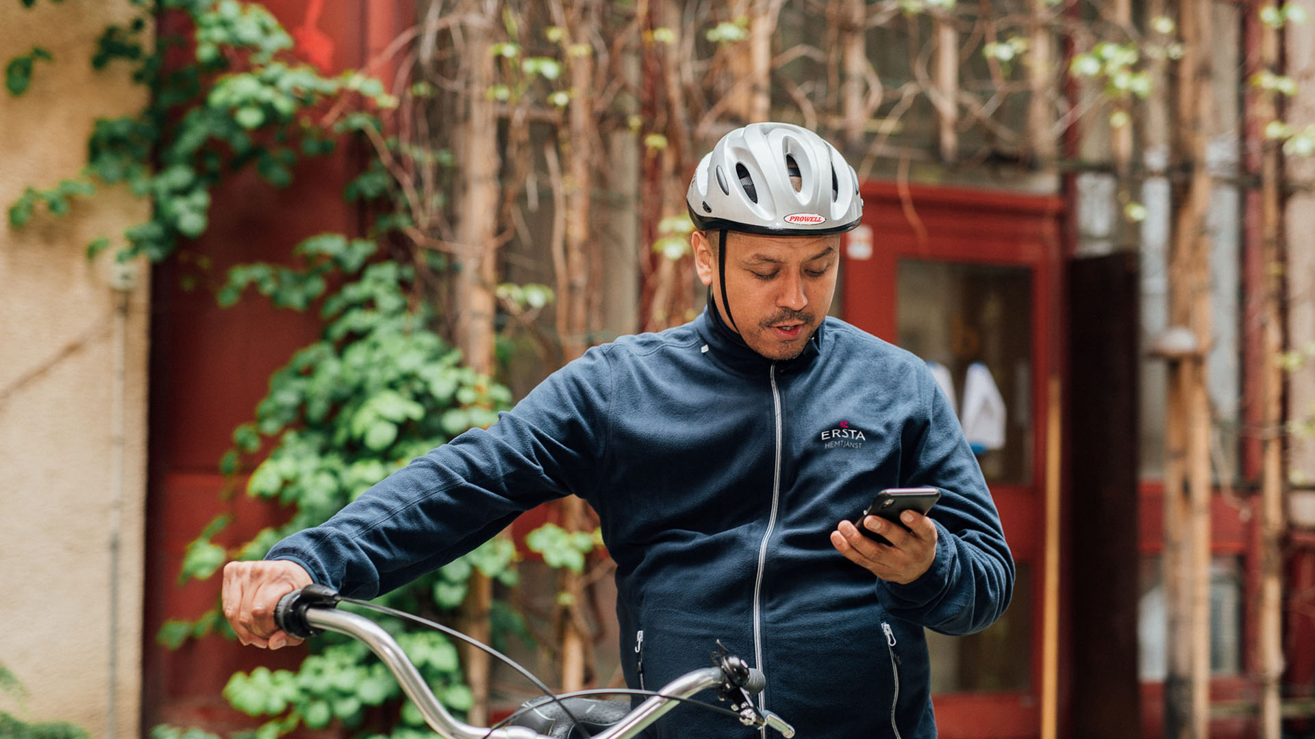 En hemtjänstmedarbetare tittar på sin telefon för att se vilken som är hans nästa kund att cykla hem till