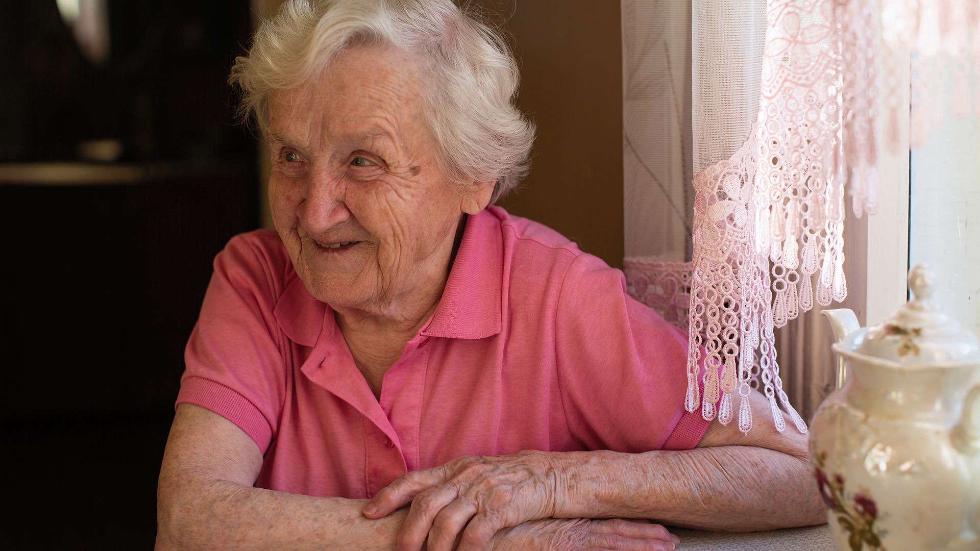 äldre kvinna i rosa tröja ler och tittar ut ur bild