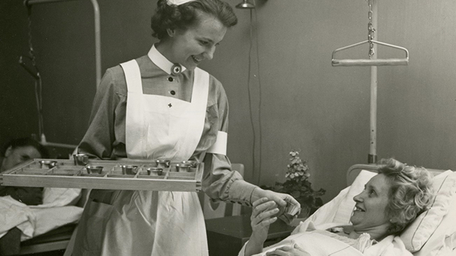 Historisk bild där sjuksyster ger kvinna i sjuksäng medicin