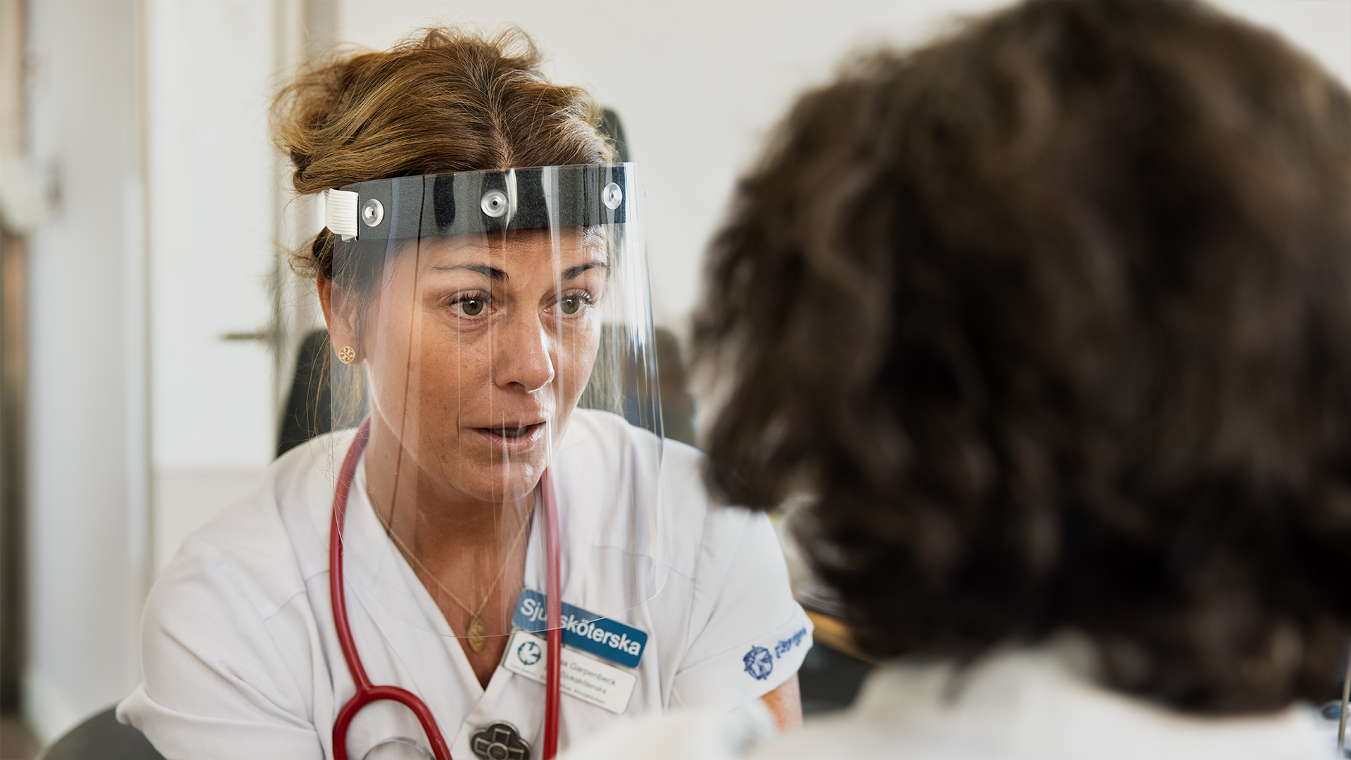 Sjuksköterska pratar med patient i ansiktsvisir