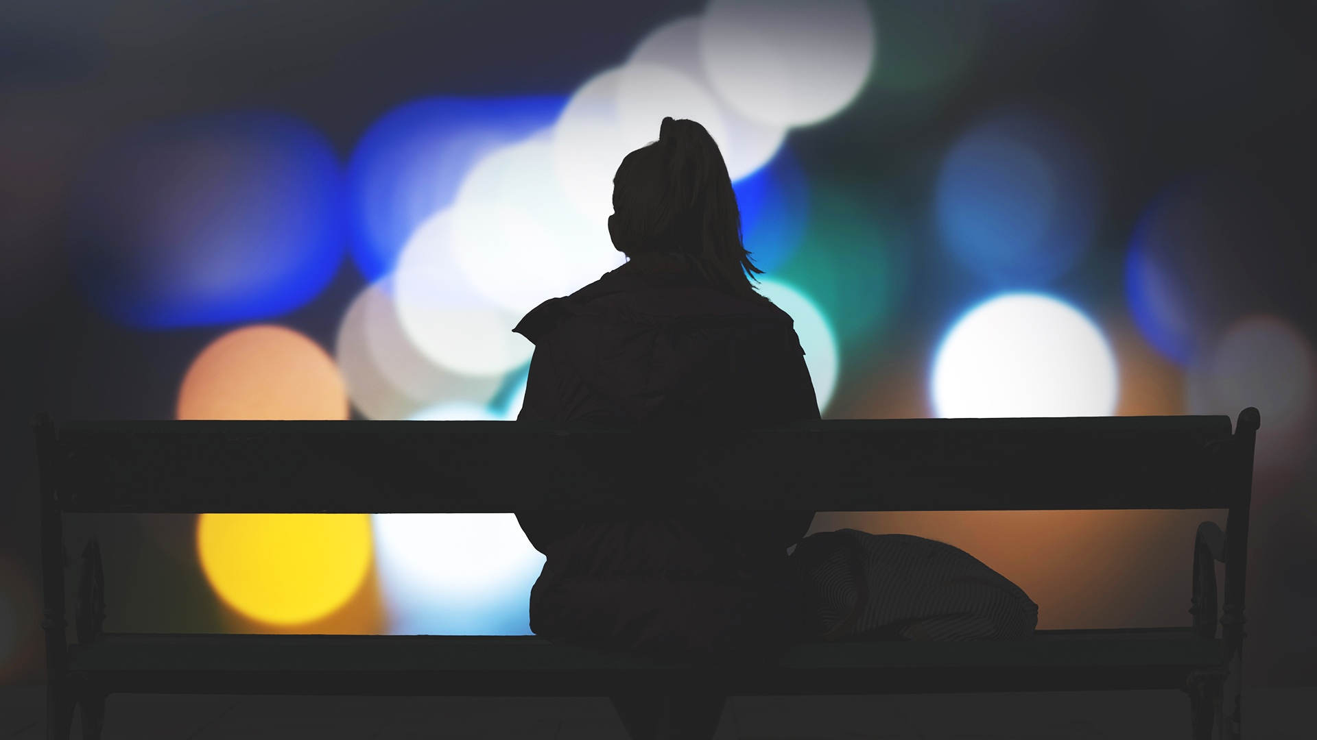 Kvinna sitter på bänk och tittar på stadens ljus