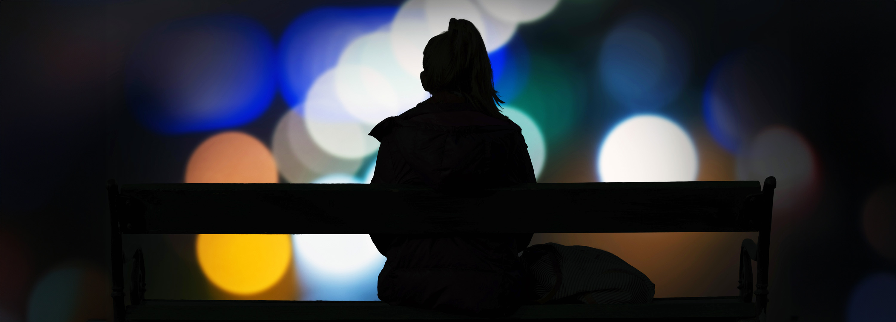 Kvinna sitter på en bänk nattetid och tittar på stadens ljus 